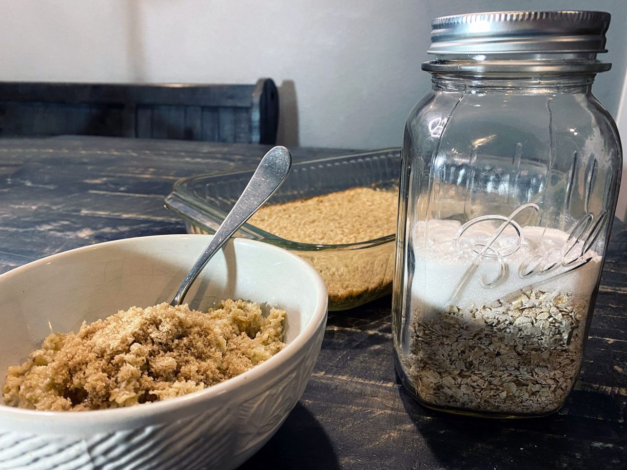 Jar of Amish baked oatmeal mix beside a baked pan of golden oatmeal served with a brown sugar topping.